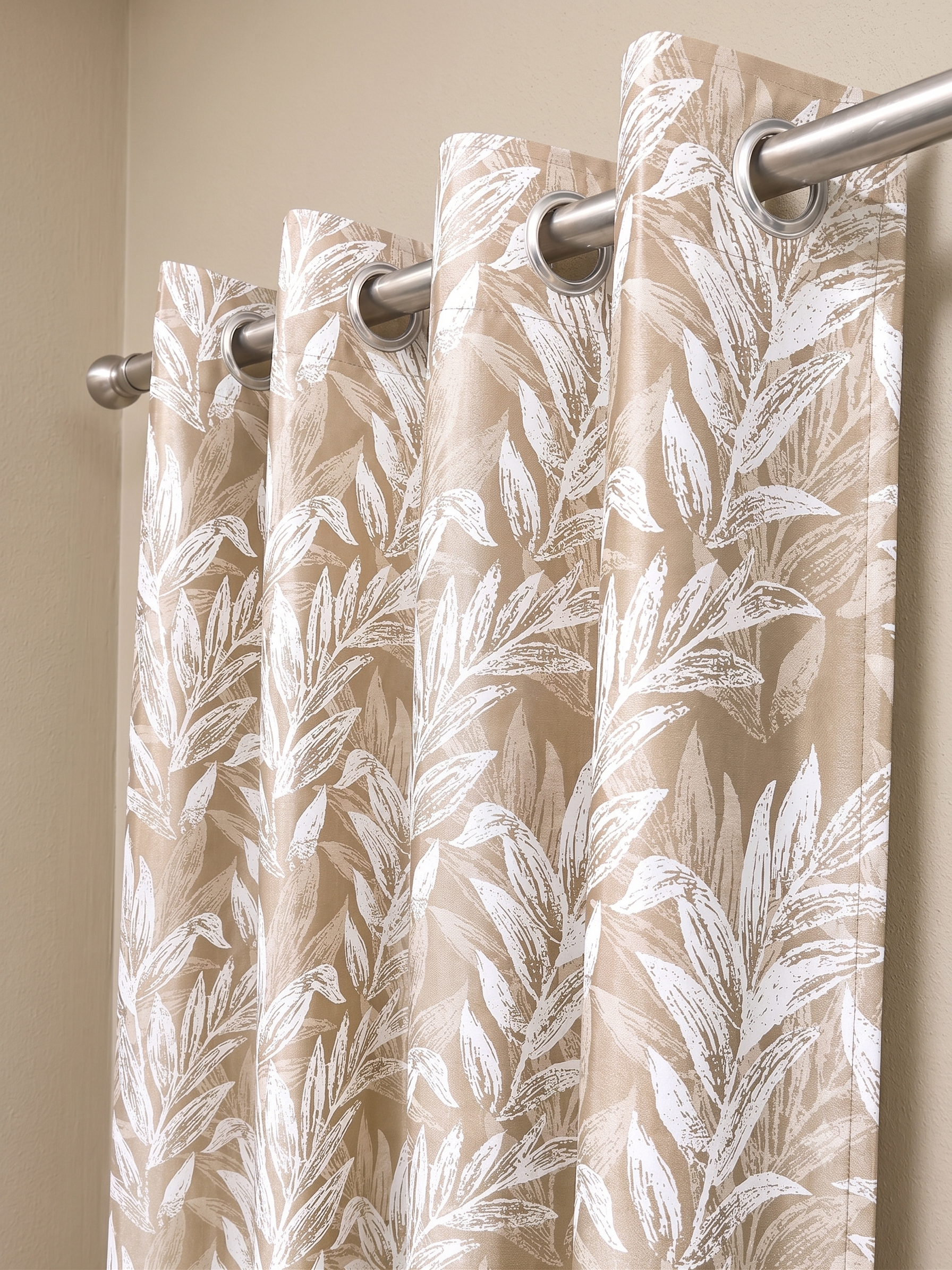 Beige floral curtain panel hanging from a steel rod on silver eyelets against a cream wall