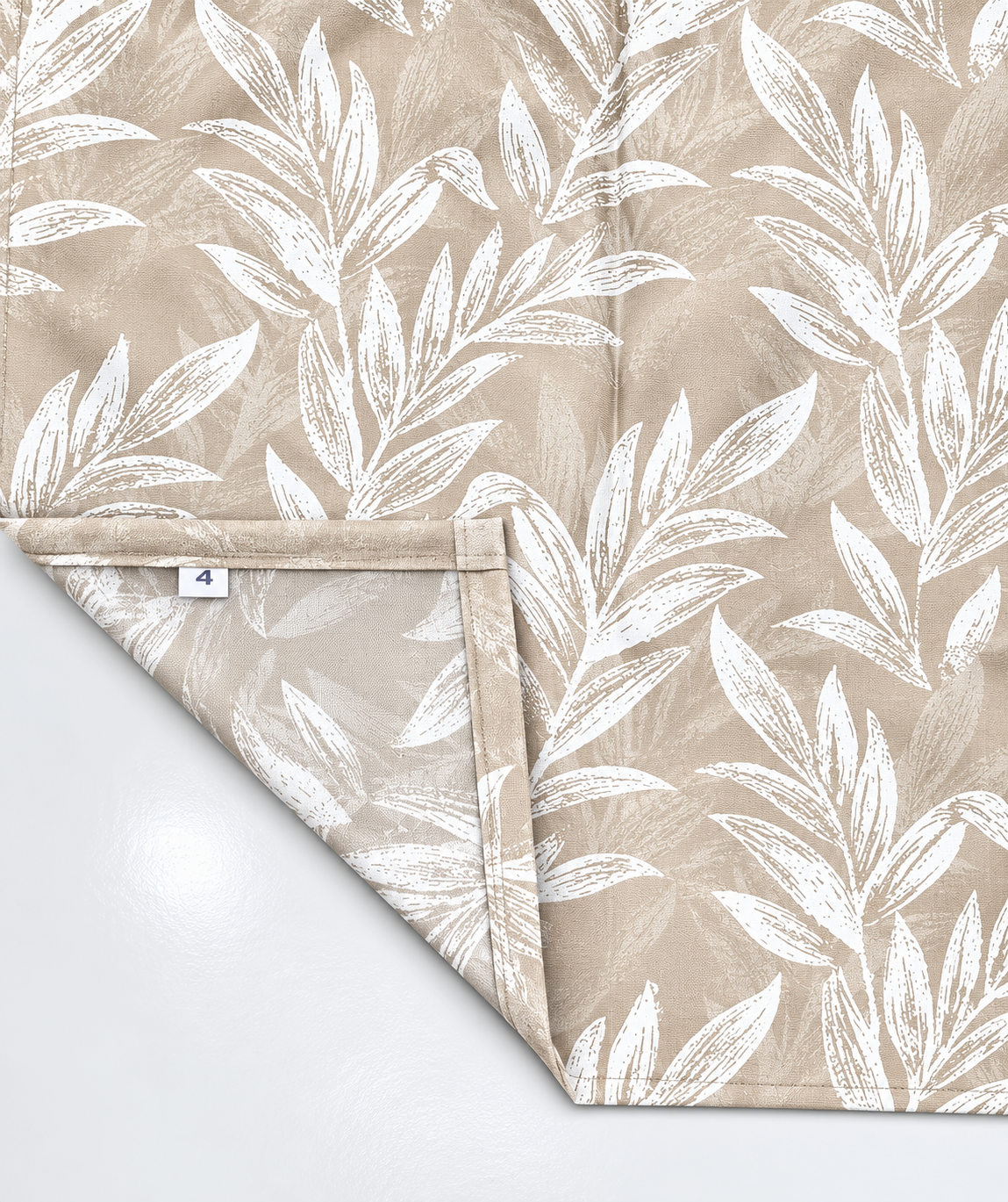 Corner of a beige floral curtain folded back to show the neatly stitched hem and woven care label