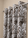 Brown floral curtain panel hanging from a steel rod on silver eyelets against a beige wall