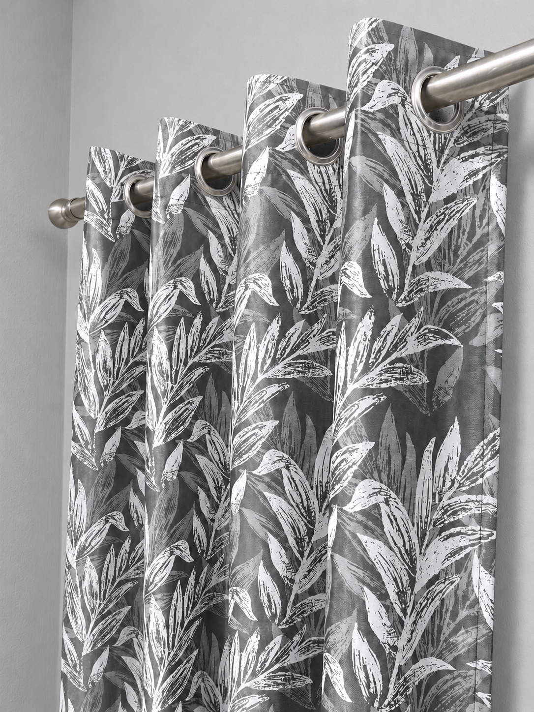 Grey floral curtain panel hanging from a steel rod on silver eyelets against a plain wall